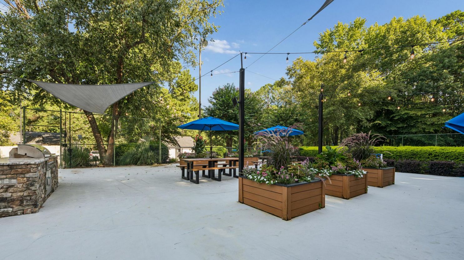 Outdoor patio with picnic tables, blue umbrellas, and wooden flower planters.