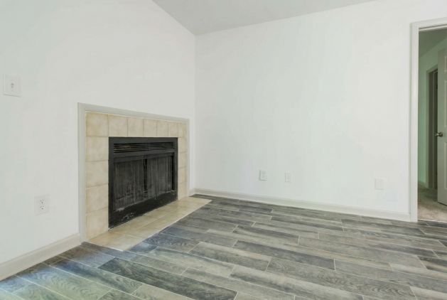 Empty room with a tiled fireplace, wood-look flooring, and white walls.