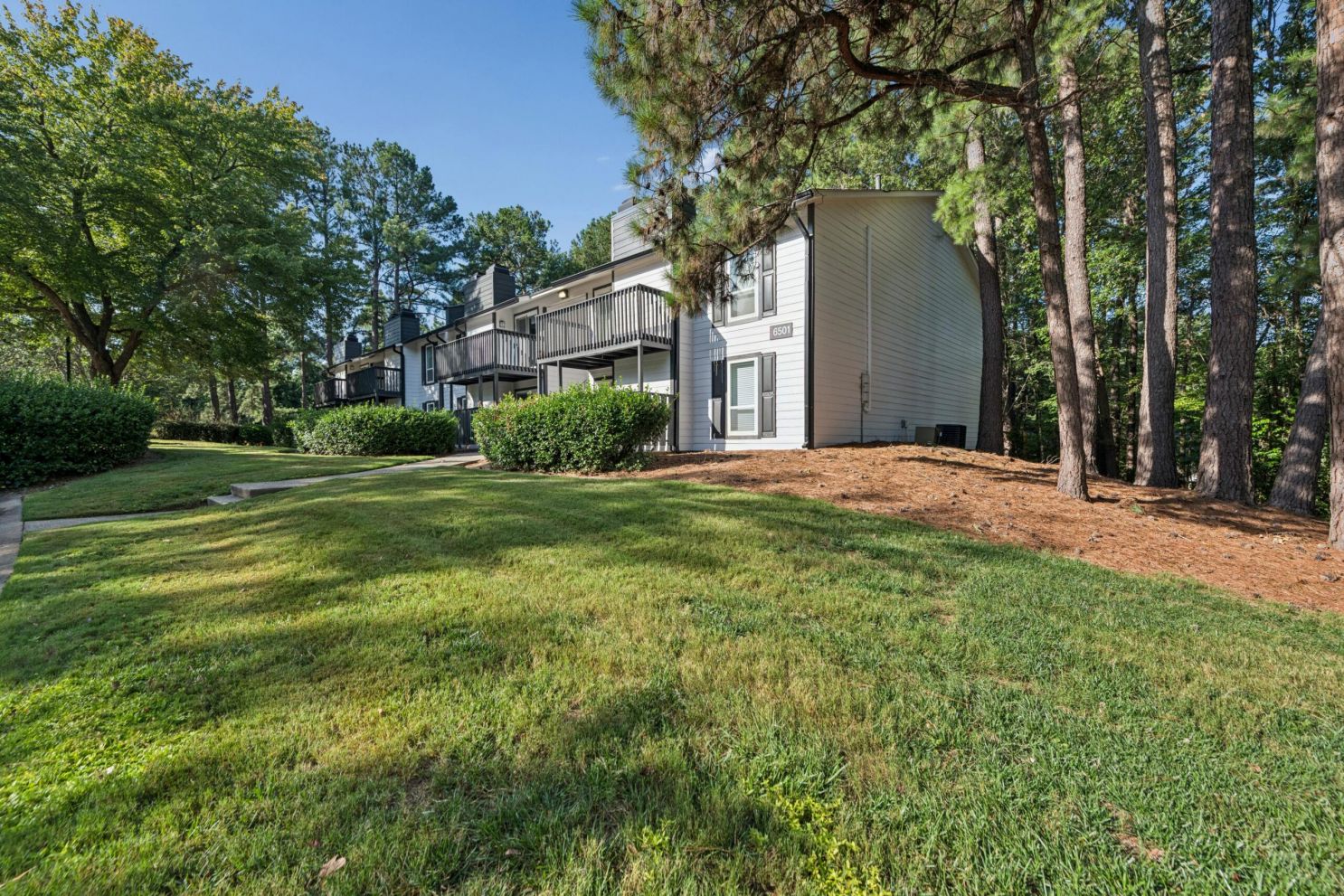Two-story apartment building with balconies surrounded by trees and a grassy lawn.